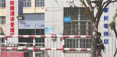  ?? NG hAN GuAN / The ASSOCIATed PreSS FILeS ?? A woman walks past a high school in Peyzawat, in western China's Xinjiang region,
where a sign warns people entering the facility to “Please speak Mandarin.”