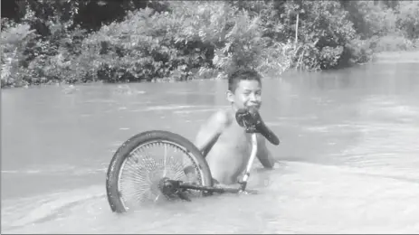  ??  ?? This boy attempted to lift his bicycle through the Kabanawau Creek to get to the other side as waters covered section of the access road to Aishalton Village.