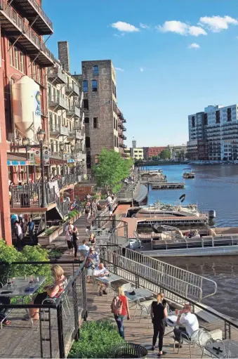  ?? ANGELA PETERSON / MILWAUKEE JOURNAL SENTINEL ?? An evening crowd enjoys dining and a scenic stroll along the RiverWalk in the Historic Third Ward on Thursday. The Third Ward segment of the RiverWalk could be completed this year. See more at jsonline.com/business.