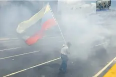  ?? ARIANA CUBILLOS/AP PHOTO ?? A man walks with a Venezuelan flag amid tear gas launched by security forces blocking opponents to President Nicolas Maduro from marching to the Ombudsman’s office in downtown Caracas, Venezuela, Wednesday. Hundreds of thousands of Venezuelan­s have...