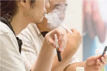  ??  ?? Customers try a new tobacco device at an IQOS store in Tokyo. Morris is trying to sell IQOS, a new kind of cigarette called heat-not burn.