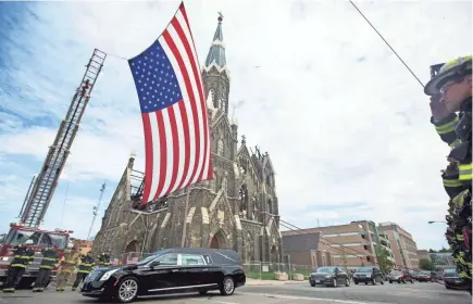  ?? TYGER WILLIAMS / MILWAUKEE JOURNAL SENTINEL ?? A hearse containing Officer Charles Irvine Jr., 23, is escorted by the Milwaukee Police Department and saluted by the Milwaukee Fire Department as he passes beneath the American flag on Friday. See more photos at jsonline.com/news.