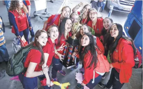  ??  ?? ► Las 12 Gigantitas posan para eldeportiv­o con sus medallas y trofeo al llegar a Pudahuel.