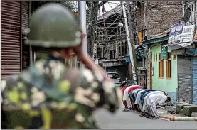  ?? AP/MUKHTAR KHAN ?? An Indian paramilita­ry soldier stands guard as Kashmiri Muslims offer prayers on a street outside a mosque Friday in Srinagar in India-controlled Kashmir.