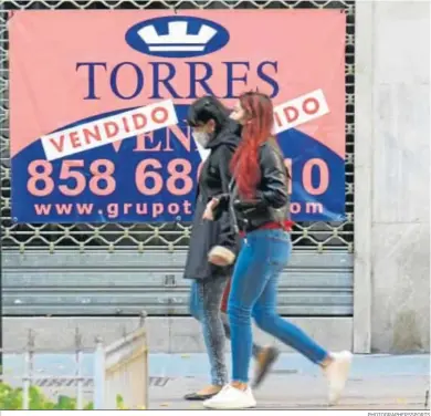  ?? PHOTOGRAPH­ERSSPORTS ?? Dos personas caminan frente al escaparate de un comercio cerrado en Granada.