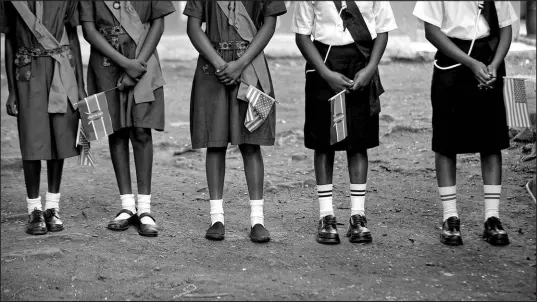  ?? BEN CURTIS / ASSOCIATED PRESS FILE (2018) ?? Kenyan girl guides holding U.S. and Kenyan f lags await the arrival of the U.S. Ambassador on March 10, 2018, at a site supported by PEPFAR, the U.S. program to fight HIV/AIDS in Africa, at the St John’s Community Centre in the Pumwani area of Nairobi, Kenya.