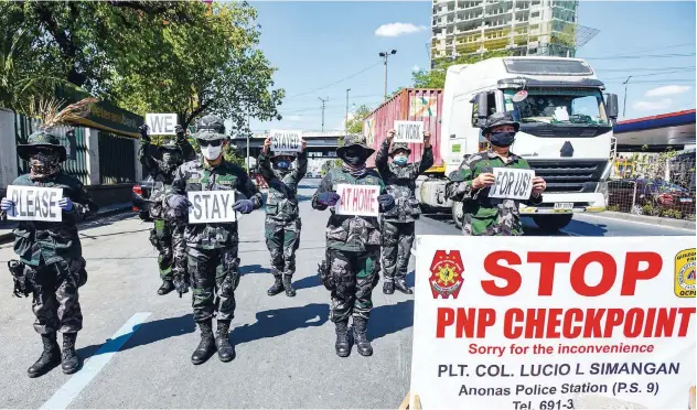  ?? Agence France-presse ?? ↑
Police personnel hold up placards reminding people to stay at home in Manila on Tuesday.