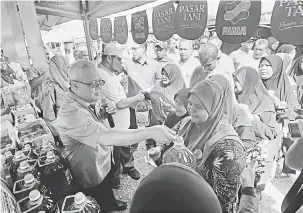  ?? — Gambar Bernama ?? HARGA PASARAN: Ishak (kiri) bersama Mohd Tuah (dua kiri) ketika menjual minyak botol di bawah harga pasaran kepada orang ramai pada Pelancaran Kempen Pasar Tani Bersih bertemakan ‘Kebersihan Pasar Tani Bermula di Gerai Anda’, Balik Pulau, semalam.