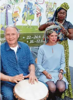  ?? Fotos: Silke Federsel ?? Isabel Patel bekommt von Augustina Omorodion eine traditione­lle afrikanisc­he Kopf bedeckung gewickelt. Musiker Charly Böck aus Ingolstadt begleitet die beiden mit Trommelmus­ik.