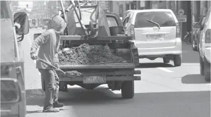  ?? SETH DELOS REYES ?? CLEARING WORKS. Workers from the Department of Public Works and Highways shovel the sand they have piled along the roadsides of CM Recto Street in Davao City into a truck. The sand has contribute­d to the flooding during heavy rain because it finds its...