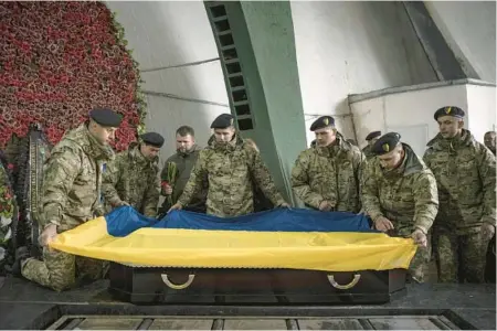  ?? JIM HUYLEBROEK/THE NEW YORK TIMES ?? Ukrainian soldiers fold a national flag over the casket of a fallen soldier Saturday in Kyiv.