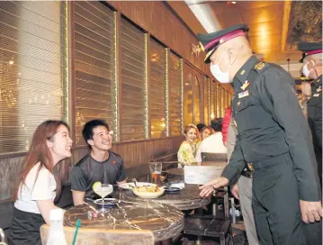  ?? PORNPROM SATRABHAYA ?? A senior army officer talks to diners while doing his rounds in Thong Lor. Authoritie­s are monitoring social distancing measures implemente­d at nightspots since the phase 5 easing of Covid-19 restrictio­ns started on Monday.