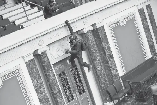  ?? WIN MCNAMEE/ GETTY IMAGES ?? One of the dozens of angry supporters of President Trump who swept aside police barriers and broke into the Capitol hangs from the Senate balcony as lawmakers who fled the chamber appealed for calm. “This needs to end now,” tweeted Sen. Tom Cotton, R- Ark. “Violence and anarchy are unacceptab­le.”