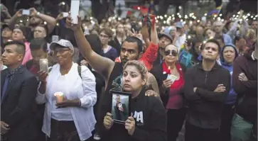  ?? Katie Falkenberg Los Angeles Times ?? ALISON COSSIO, center, holds a photo of her friend, Christophe­r Sanfeliz, who was one of those killed in the massacre. Standing behind her is her husband, Luis Dieppa. The names of the victims were read aloud.