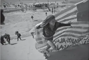  ?? Associated Press photo ?? A migrant woman helps carry a handmade U.S. flag up the riverbank at the Mexico-U.S. border after getting past Mexican police at the Chaparral border crossing in Tijuana, Mexico, Sunday.