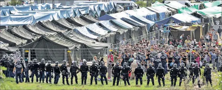  ?? ZOLTAN GERGELY KELEMEN / AP ?? Un cordón policial frente a centenares de personas concentrad­as en el campo húngaro de Rószke, cerca de la frontera con Serbia, del que escaparon ayer unas trescienta­s