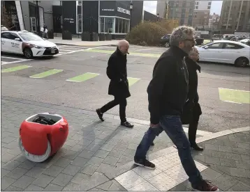  ?? PHOTOS BY MATT O’BRIEN — THE ASSOCIATED PRESS ?? Piaggio Fast Forward CEO Greg Lynn, center, is followed by his company’s Gita carrier robot as he crosses a street Nov. 11in Boston. The two-wheeled machine is carrying a backpack and uses cameras and sensors to track its owner.