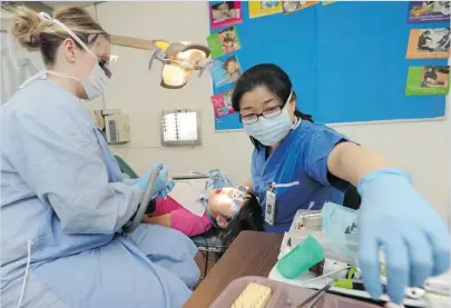  ?? JASON PAYNE/ PNG ?? Dental assistant Natasha Tibbo ( left) and dentist Sarah Park give a Florence Nightingal­e elementary school student a checkup. UBC Faculty of Dentistry students provide dental care twice a month at the school.