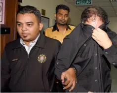  ??  ?? Badaruddin covers his face as he is led to the courtroom. — Bernama photo