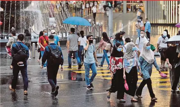  ?? PIC BY AIZUDDIN SAAD ?? People wearing face masks cross the street on a rainy day in Kuala Lumpur yesterday.