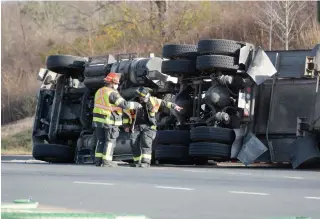  ?? DAVE JOHNSON TORSTAR ?? Welland Fire and Emergency Services firefighte­rs look over the underside of a transport truck resting on its side in the eastbound lanes of the East Main Street roundabout Wednesday.