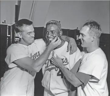  ?? Mark Rucker Getty Images ?? BROOKLYN DODGERS first baseman Jackie Robinson, center, receives congratula­tions from winning pitcher Clem Labine, left, and starting pitcher Carl Erskine after a game at Ebbets Field on July 31, 1956.