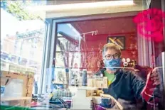  ?? Alexandra Wimley/Post-Gazette ?? Bernadette Gerbe, the owner and glass artist at Gerbe Glass, sews face masks in the window of her shop Monday in Lawrencevi­lle. She is giving masks away to anyone who stops by, asking only for a $1 donation to cover the cost of supplies.