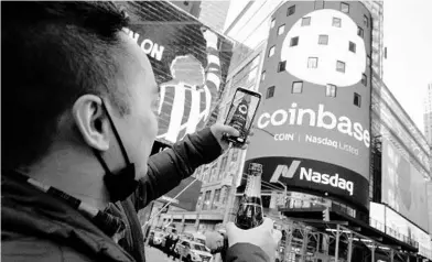  ?? RICHARD DREW/AP ?? Coinbase employee Daniel Huynh holds a bottle of Champagne as he takes a picture Wednesday outside the Nasdaq MarketSite in New York’s Times Square. The digital currency exchange became a publicly traded company earlier this week.