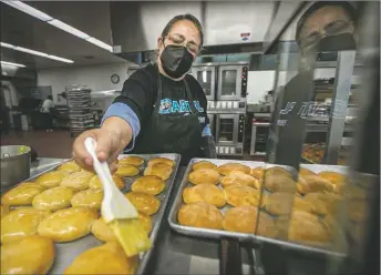  ?? JIM WEBER/The New Mexican ?? Olivia Ponce butters rolls and buns last week as cafeteria staff at Capital High School prepare for lunch.