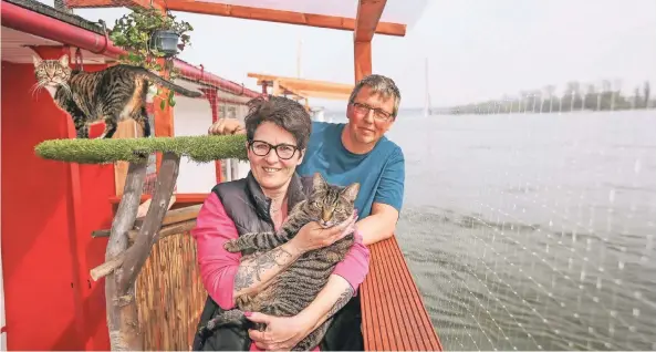  ??  ?? Ganz nah am Wasser: Laura und Stefan Bottke (mit Leo und Lilli) leben auf dem Fluss. Das feine Netz auf der Terrasse soll verhindern, dass die beiden Katzen baden gehen.