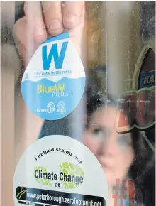  ?? SPECIAL TO THE EXAMINER ?? GreenUP water programs coordinato­r Jenn McCallum places a Blue W Ptbo decal in the window at Black Honey Café on Hunter St. Look for the decal at local businesses and public service buildings, marking them as destinatio­ns for refilling up your reusable...