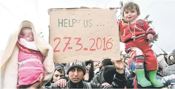  ??  ?? Migrants with their children protest next to a placard reading ‘help us’, in front of anti-riot police at the makeshift camp of the GreekMaced­onian border, near the Greek village of Idomeni, where thousands of refugees and migrants are stranded by the...