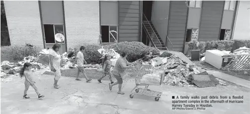  ?? AP Photo/David J. Phillip ?? A family walks past debris from a flooded apartment complex in the aftermath of Hurricane Harvey Tuesday in Houston.