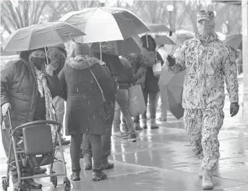  ?? MICHAEL M. SANTIAGO/GETTY ?? A National Guard soldier enforces social distancing as people withstand poor weather while waiting in line Friday to enter the COVID-19 vaccinatio­n site at Yankee Stadium in the Bronx borough of New York City.