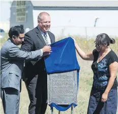  ?? BRANDON HARDER ?? Janine Windolph, right, Gene Makowsky, Minister of Parks, Culture and Sport, centre, and land owner Nadeem Islam unveil a plaque at the Regina Indian Industrial School Cemetery on Pinkie Road.