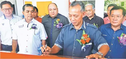  ??  ?? Penguang (second right) signs the plaque to declare open the new market as (from right) Alexander, Angki, Allan, Aaron and others look on.