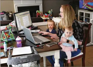  ?? PHOTOS BY CURTIS COMPTON / CCOMPTON@AJC.COM ?? Samantha Gygax makes decisions about product supply and demand as she tries to occupy daughters Josephine, 2, and Kathryn, 6 months, while working from the kitchen of her Roswell home Tuesday. Gygax is the demand planner for High Road Craft Ice Cream.