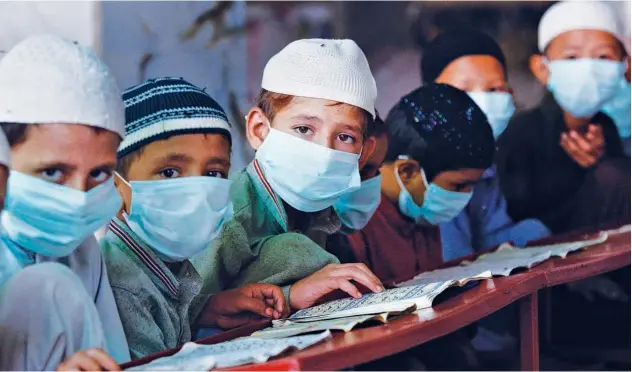  ?? Associated Press ?? ↑
Children, wearing face masks, read the Holy Quran at a religious school in Karachi on Saturday.