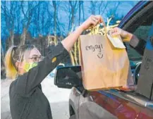  ??  ?? Kamryn Tisdel, a server at Killarney House, delivers a meal and drinks curbside to customer Jack Stump. Many customers have become used to ordering cocktails with their carryout meals from restaurant­s during the pandemic.