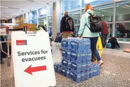  ?? ?? A sign directing wildfire evacuees to services available to them stands next to a pallet of bottled water Friday at the airport in Calgary, Alberta. The evacuation orders in Northwest Territorie­s and British Columbia marked the latest chapter of a terrible summer for wildfires in Canada, with tens of thousands of people forced to leave their homes and vast swaths of land scorched.