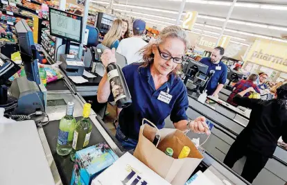  ?? [PHOTO BY NATE BILLINGS, THE OKLAHOMAN] ?? Beverly Beddoe bags a bottle of wine before scanning a customer’s other groceries inside the Homeland store at Classen and NW 18 on Monday, the first day of wine and strong beer sales in grocery stores.