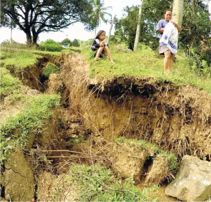  ?? SUNSTAR FOTO / ALAN TANGCAWAN ?? CRACKED. A mother and her child watch a huge gap in the soil caused by landslides that followed heavy rains in the city the past week.