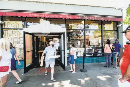  ?? Noah Berger / Special to The Chronicle ?? Customers line up for takeout orders at Arizmendi Bakery in Oakland, where cases are spiking in Black and Latino areas.