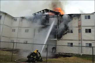  ?? Herald photo by Tim Kalinowski ?? Firefighte­rs pour water on a blaze at the 300 block of Highlands Boulevard West Friday morning. Thirty-six units in the apartment were severely damaged in the fire, which officials say started on a second-floor outside balcony and spread up onto the roof.