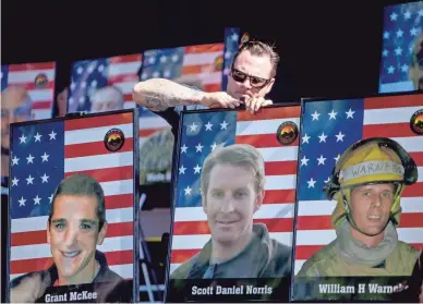  ?? PHOTOS BY BRIAN MUNOZ/THE REPUBLIC ?? Prescott firefighte­r Lance Mills adjusts the portraits of the 19 firefighte­rs killed in the 2013 Yarnell Hill Fire on Saturday during a memorial ceremony for the Granite Mountain Hotshots in downtown Prescott. It is still the deadliest day for U.S. firefighte­rs since Sept. 11.