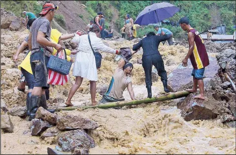  ?? ANDY ZAPATA JR. ?? Miners help residents cross a flooded main road in Virac, Itogon, Benguet yesterday following heavy rains which triggered a landslide.