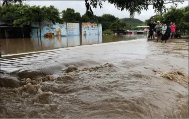  ?? DELMER MARTINEZ — THE ASSOCIATED PRESS ?? People stand on the edges of a flooded street after the passing of Iota Nov. 18 in La Lima, Honduras. Iota flooded stretches of Honduras still underwater from Hurricane Eta, after it hit Nicaragua Monday evening as a Category 4 hurricane and weakened as it moved across Central America, dissipatin­g over El Salvador early Wednesday.