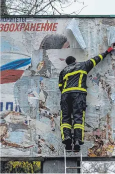  ?? FOTO: BERNAT ARMANGUE/DPA ?? Nach dem Abzug der Russen aus Cherson reißt ein ukrainisch­er Feuerwehrm­ann ein russisches Werbeplaka­t von einer Tafel.