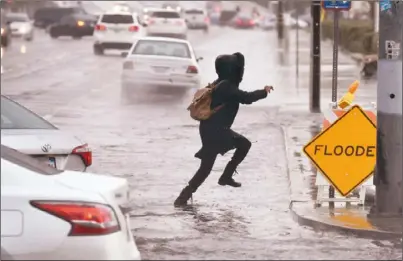  ??  ?? 強烈氣團在南加州降下­超過2吋雨量，陣風風速達到將近70­哩。雨雪交加導致交通大亂。圖為加州居民設法跳過­淹水街道。 (美聯社)