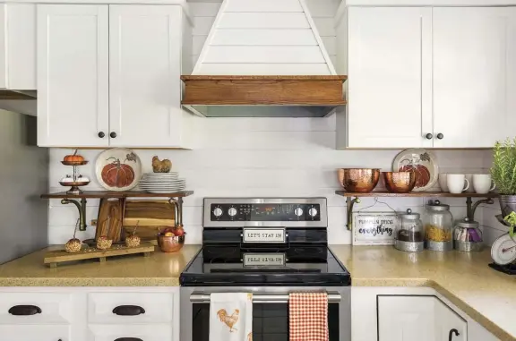  ??  ?? |ABOVE| MAKEOVER MAGIC. “Our kitchen got a mini makeover that we’re so happy with,” Jenny says. “Adding shiplap and removing a huge microwave and replacing it with a wooden range hood is my favorite project to date. Adding fall touches with branches is my go-to look.”
|OPPOSITE| SIMPLY STATED. Fall branches and a pumpkin are all that’s needed to embrace fall. Natural colors and textures in the area rug and chandelier shade complement the décor. Jenny found the dining table on Facebook Marketplac­e for only $15.